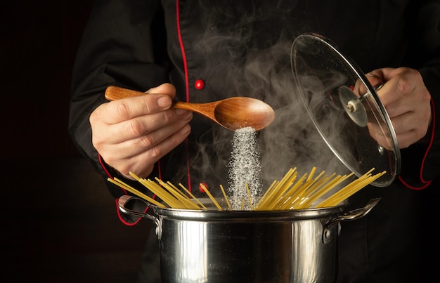 the cook adds a spoonful of salt to a boiling pot of spaghetti free space for recipe or menu on dark background