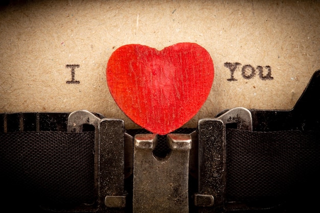 Ti amo frase sulla macchina da scrivere Concetto di saluti di San Valentino Piccolo cuore di legno rosso primo piano Biglietto di auguri di San Valentino
