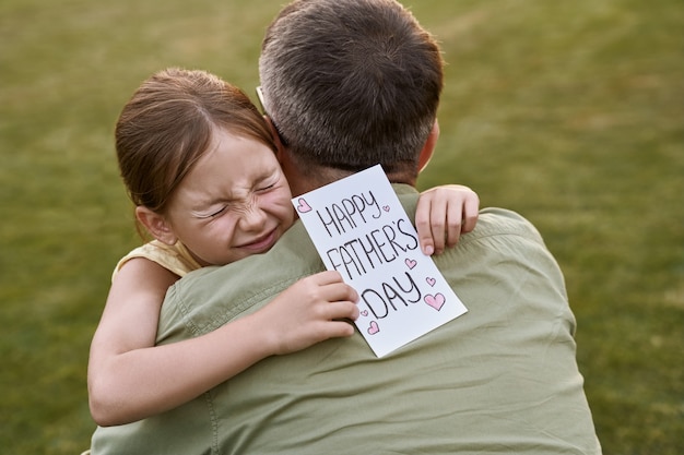 Ti amo papà, bambina felice e carina, piccola figlia che abbraccia suo padre e gli dà una cartolina