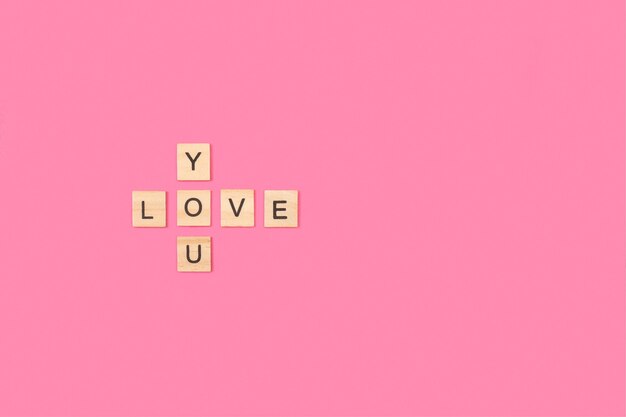 Ti amo scrivere con blocchi di lettere in legno su uno sfondo rosa