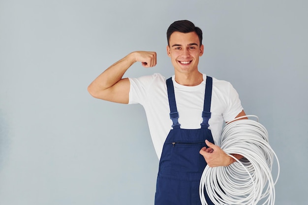 Tiene il cavo Lavoratore maschio in uniforme blu in piedi all'interno dello studio su sfondo bianco