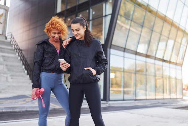 Tiene il telefono in mano Due amiche con corpi sportivi hanno una giornata di fitness all'aperto