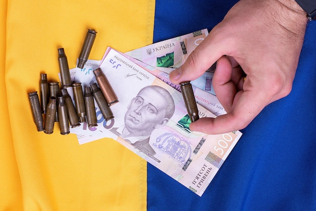 Tiene in mano banconote e bossoli di grivna su uno sfondo diviso per metà da una bandiera ucraina blu e gialla concetto di acquisto di armi da altri paesi