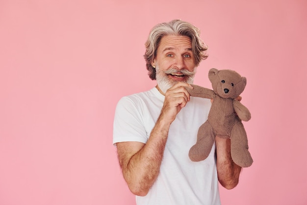 Tiene l'orsacchiotto L'uomo anziano moderno e alla moda con i capelli grigi e la barba è al chiuso