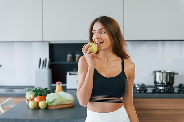 Tiene la mela in mano La giovane donna europea è al chiuso in cucina al chiuso con cibo sano