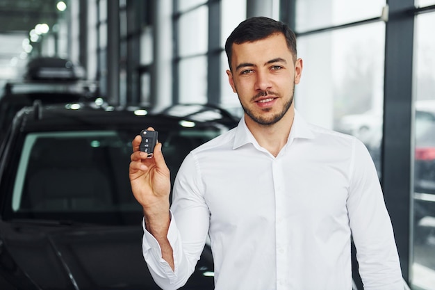 Tiene le chiavi Il giovane in camicia bianca è al chiuso con una nuova automobile moderna