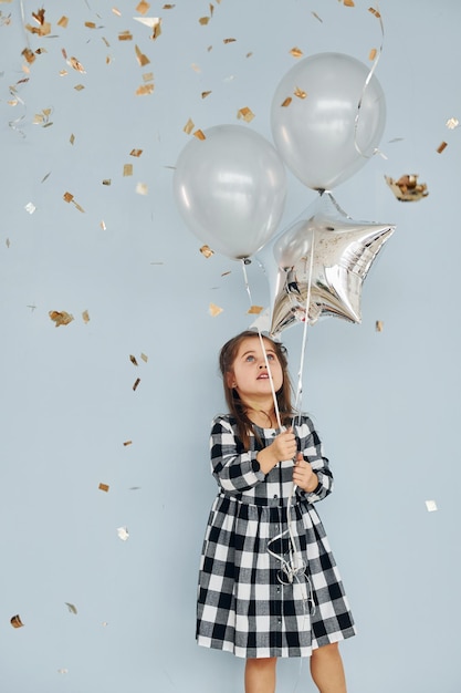 Tiene palloncini Bambina felice in piedi e divertirsi al chiuso alla festa di compleanno