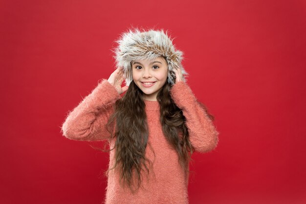 Tieni la testa al caldo. Sensazione di caldo. Cappello morbido da bambino a pelo lungo. Concetto di moda invernale. Cappello caldo per il freddo inverno. Priorità bassa rossa della ragazza del bambino. Accessorio in morbido pelo. Stagione invernale. Concetto di acquisto.