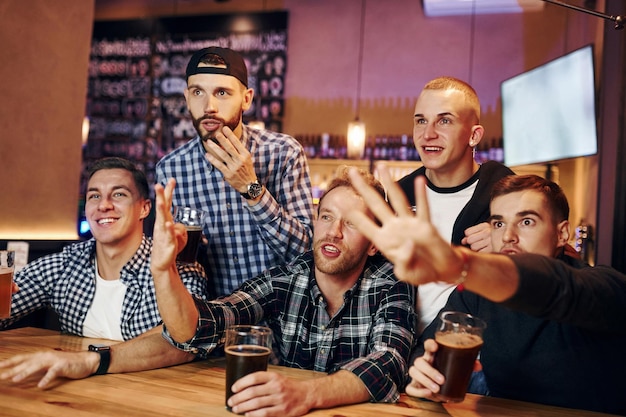 Tifosi di calcio che guardano la TV Gruppo di persone insieme al chiuso nel pub si divertono durante il fine settimana