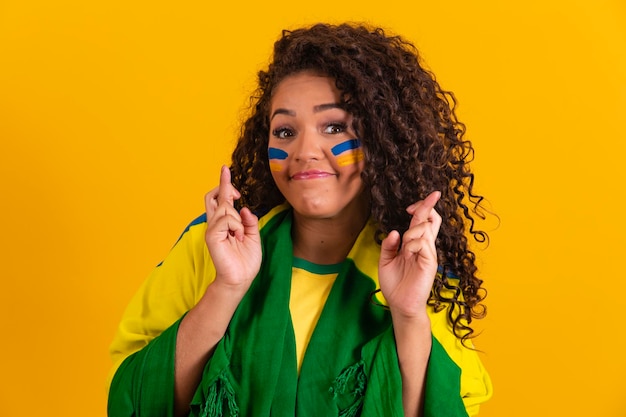 Tifoso brasiliano con dita incrociate che vibra fortuna su sfondo giallo