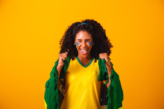 Tifoso brasiliano. indossando la bandiera brasiliana in un ritratto, fan brasiliano che celebra il calcio o la partita di calcio su sfondo giallo. I colori del Brasile.Coppa del mondo