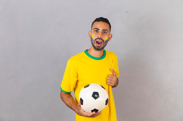 Tifoso brasiliano su sfondo grigio che celebra la vittoria in possesso di un pallone da calcio