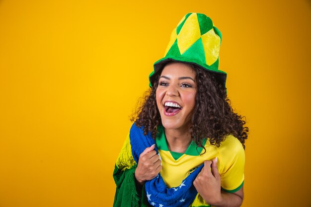 Tifoso del Brasile. Fan brasiliano della donna dei capelli ricci che celebra sul calcio, partita di calcio su fondo giallo. Colori del Brasile.