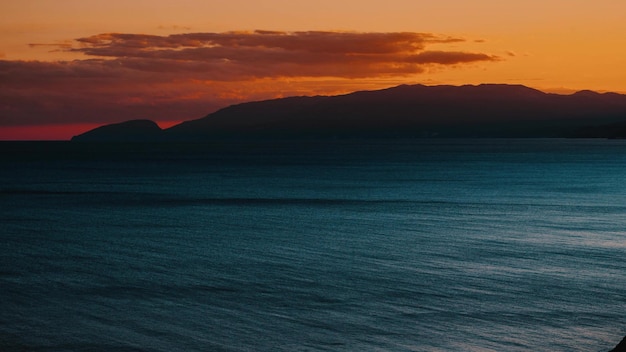 Timelapse di drammatico tramonto arancione sul mare con le montagne la sera d'estate