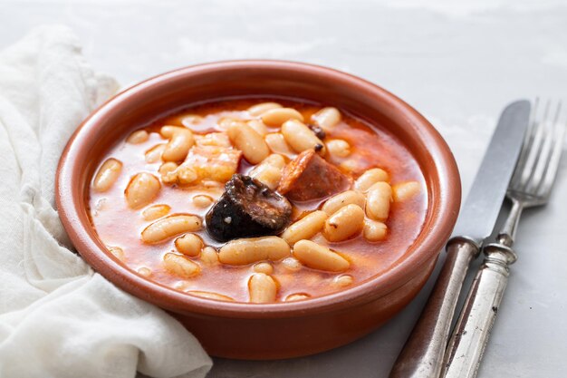 Tipico piatto spagnolo fabada, fagioli con salsicce affumicate e carne su piatto di ceramica marrone