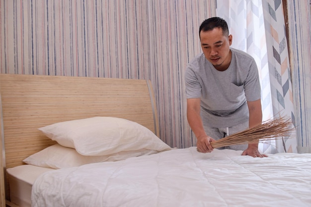Tipo asiatico che fa il letto al mattino usando una scopa tradizionale o un detergente per materassi