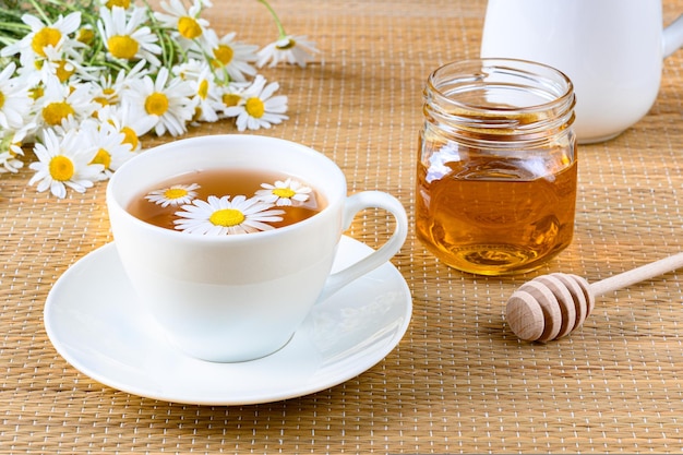 Tisana con fiori di camomilla in tazza lattiera e miele su stuoia in rattan