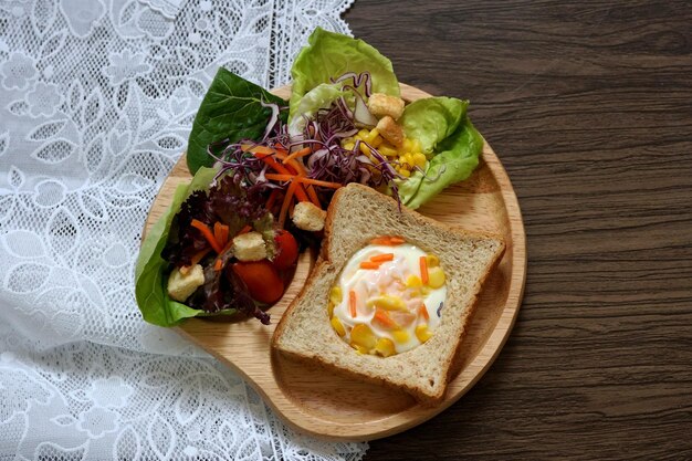 Toast all'uovo con insalata mista per la colazione su un piatto di legno.