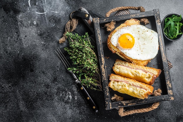 Toast alla francese croque monsieur e croque madame con prosciutto a fette formaggio emmental fuso e uova Sfondo nero Vista dall'alto Spazio di copia