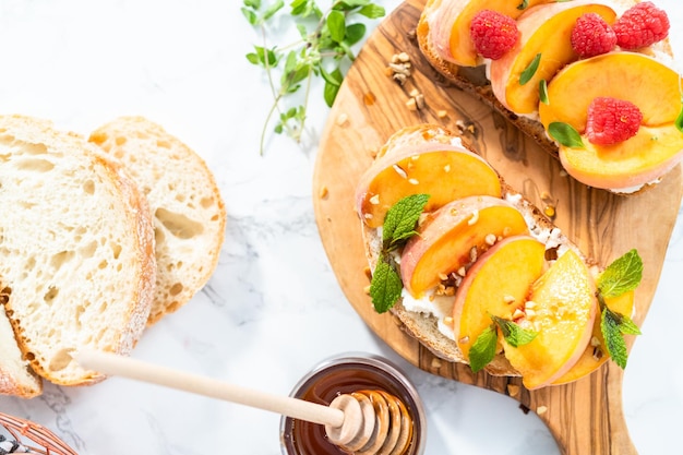 Toast alla ricotta e pesca guarniti con noci, menta fresca e lamponi su un tagliere di legno.