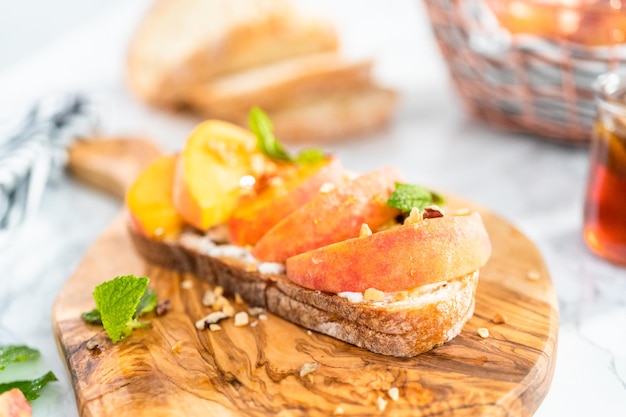 Toast alla ricotta e pesca guarnito con noci e menta fresca su un tagliere di legno.