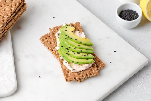 Toast con avocado fresco e formaggio su pane a bordo bianco. Fotografia leggera