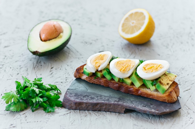 Toast con avocado, limone, peperoncino o paprika e uova su uno sfondo grigio