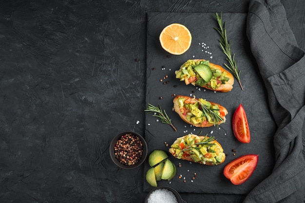 Toast con avocado, pomodoro e rosmarino su un tavolo di cemento nero. Vista dall'alto, con spazio per copiare. Il concetto di corretta alimentazione.