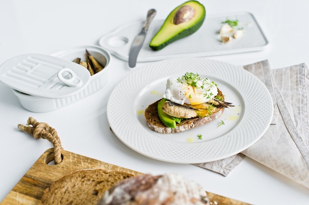 Toast con avocado, uovo in camicia e spratti.