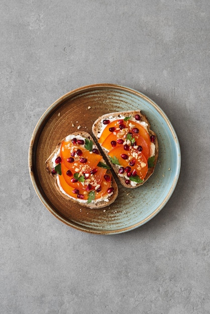 Toast con formaggio crema persimmon e semi di melograno su uno sfondo di cemento concetto fotografico alimentare minimalista