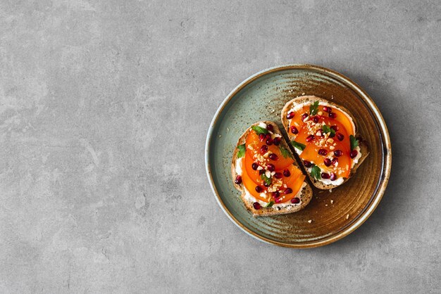 Toast con formaggio crema persimmon e semi di melograno su uno sfondo di cemento concetto fotografico alimentare minimalista