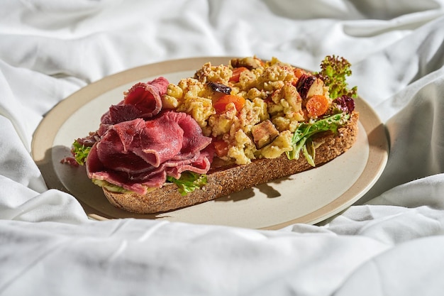 Toast con roast beef uova strapazzate su un piatto su un foglio bianco Luce dura