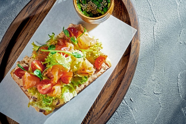 Toast con salmone, pomodorini e lattuga su una tavola di legno Sfondo concreto luce del mattino Cibo per la colazione Vista dall'alto