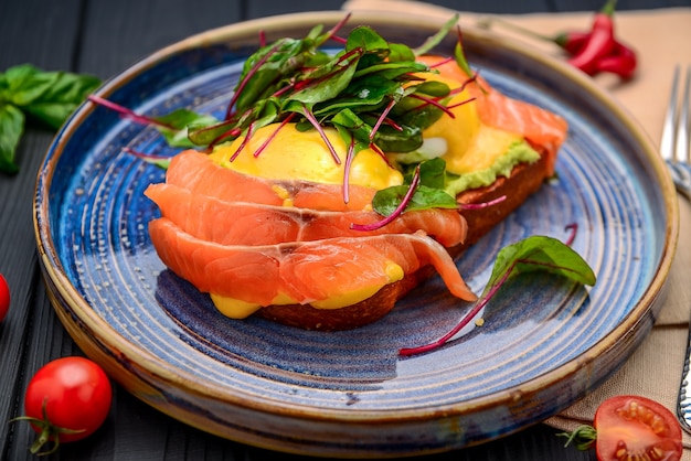 Toast con salmone, uovo in camicia e avocado su un piatto. Prima colazione al ristorante