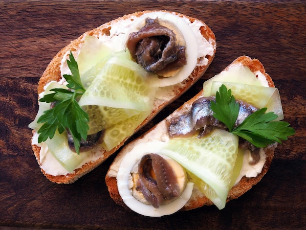 Toast con uovo di cetriolo e acciughe su un tagliere bianco