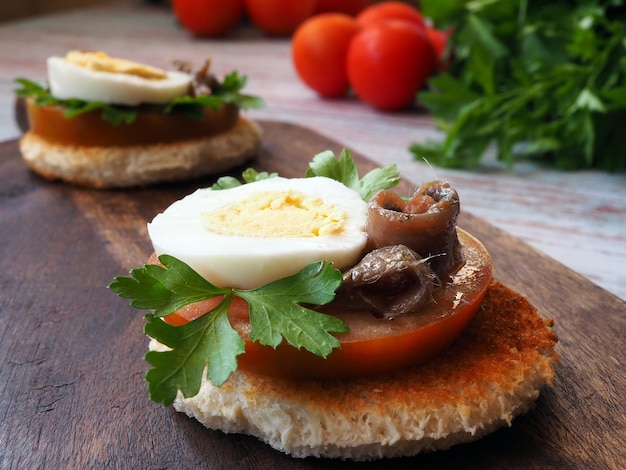 Toast con uovo di pomodoro e acciughe su una tavola di legno