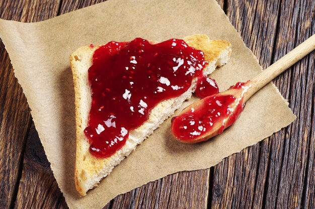 Toast del primo piano con marmellata di lamponi su un tavolo di legno vintage