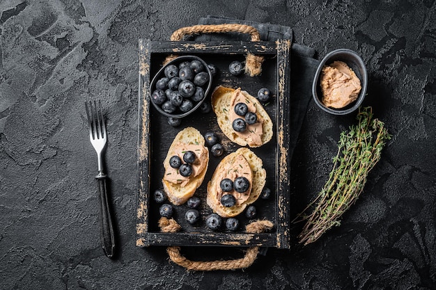 Toast di foie gras, patè di fegato d'anatra e mirtilli freschi in vassoio di legno. Sfondo nero. Vista dall'alto.