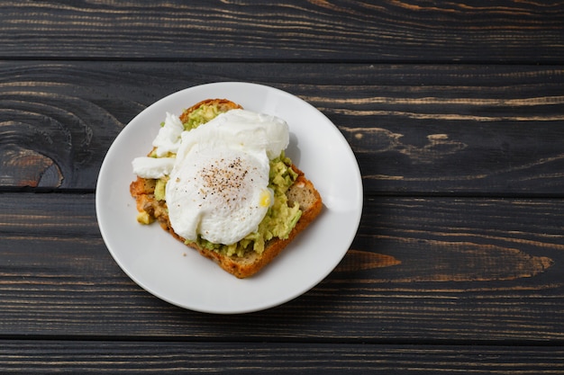 Toast e uovo in camicia con avocado su un piatto sulla tavola di legno