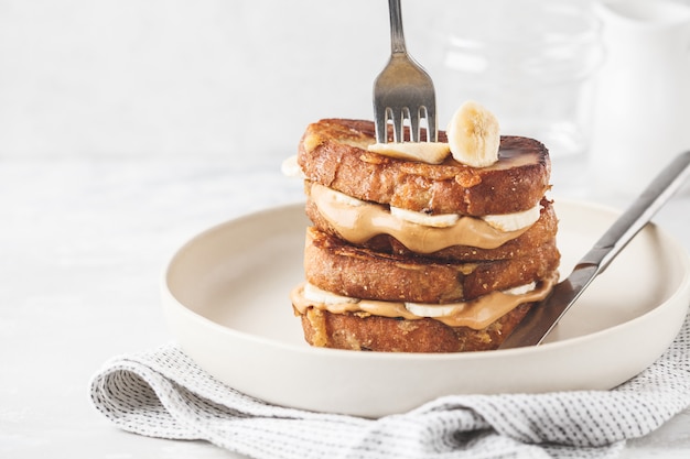 Toast francesi con burro di arachidi e banana su un piatto bianco.