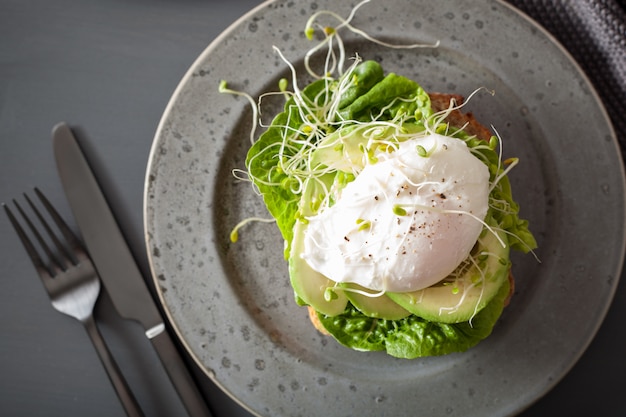 Toast per la colazione con uovo in camicia di avocado e germogli di erba medica