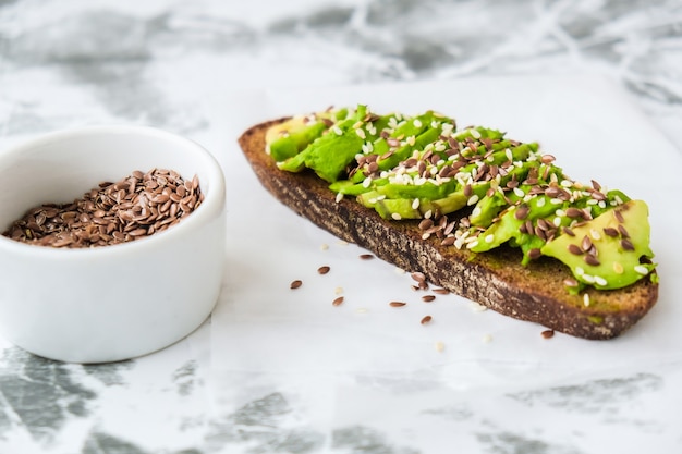 Toast sano dell'avocado su fondo concreto. Pane integrale, semi di lino al sesamo. Dieta cheto vegana. Mangiare sano. Panino vegetariano alla moda con guacamole.