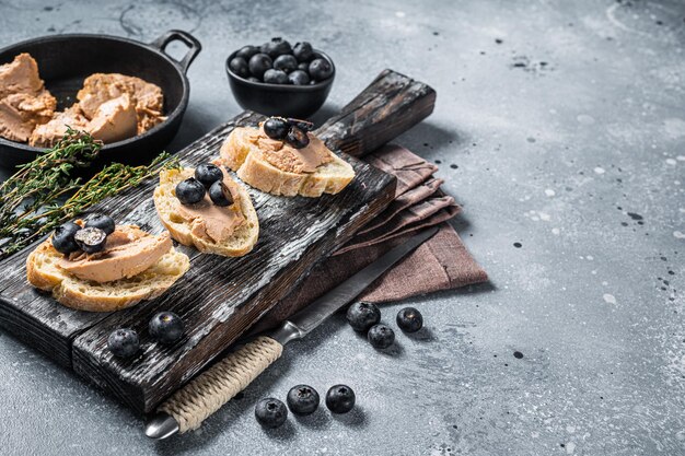 Toast with Foie gras pate and fresh blueberry on wooden board. Gray background. Top view. Copy space.