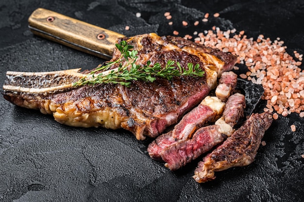 Tomahawk alla griglia invecchiato a secco o bistecca di carne di manzo da cowboy su una mannaia di carne Sfondo nero Vista dall'alto