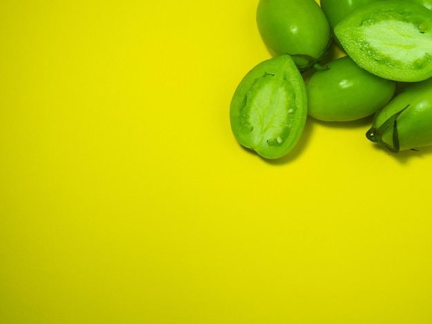 Tomati verdi su uno sfondo giallo Il concetto di una verdura immatura Sfondio di verdure verdi Alimento sano Luogo per scrivere testo