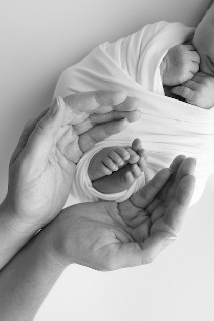 Tonalità in bianco e nero bella forma le mani della madre tengono i piccoli piedi del neonato su sfondo bianco con amore cura la sicurezza e la protezione della famiglia bambino con il concetto di nascita prematura o la cura della terapia intensiva neonatale