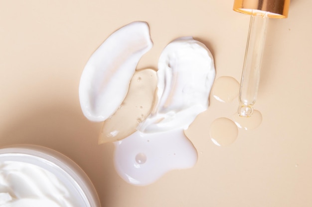 Top gocce e macchie di cosmetici con una pipetta e un vasetto di crema su fondo beige