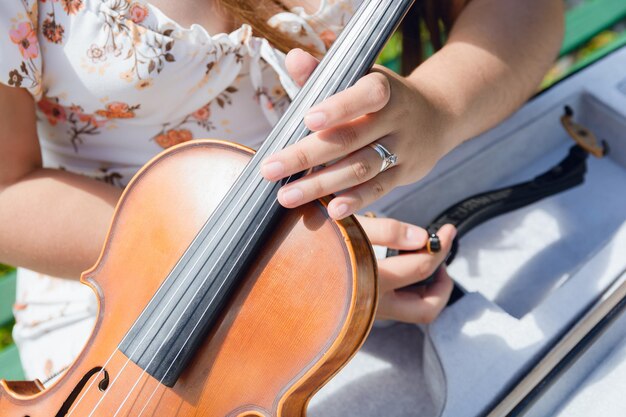 top view close-up di una donna irriconoscibile che tiene in mano un violino con una mano e lo tira fuori dal caso all'aperto