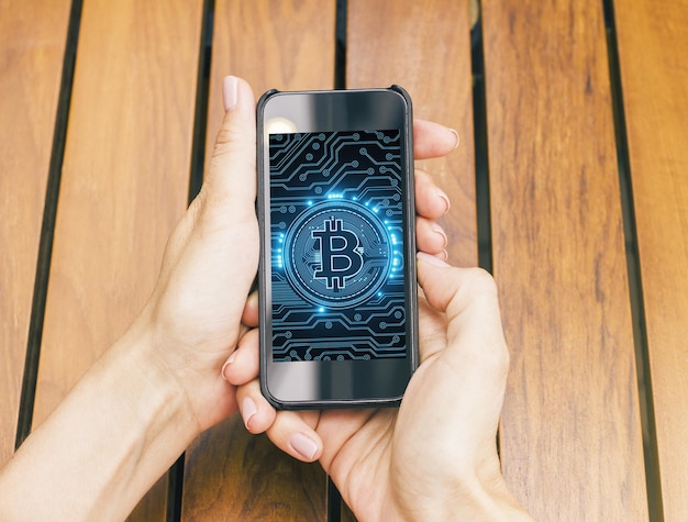 top view of female hands holding cellphone with bitcoin screen at wooden desk web and network concept