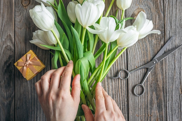 Top view un bouquet di tulipani bianchi in mani femminili forbici e una scatola regalo